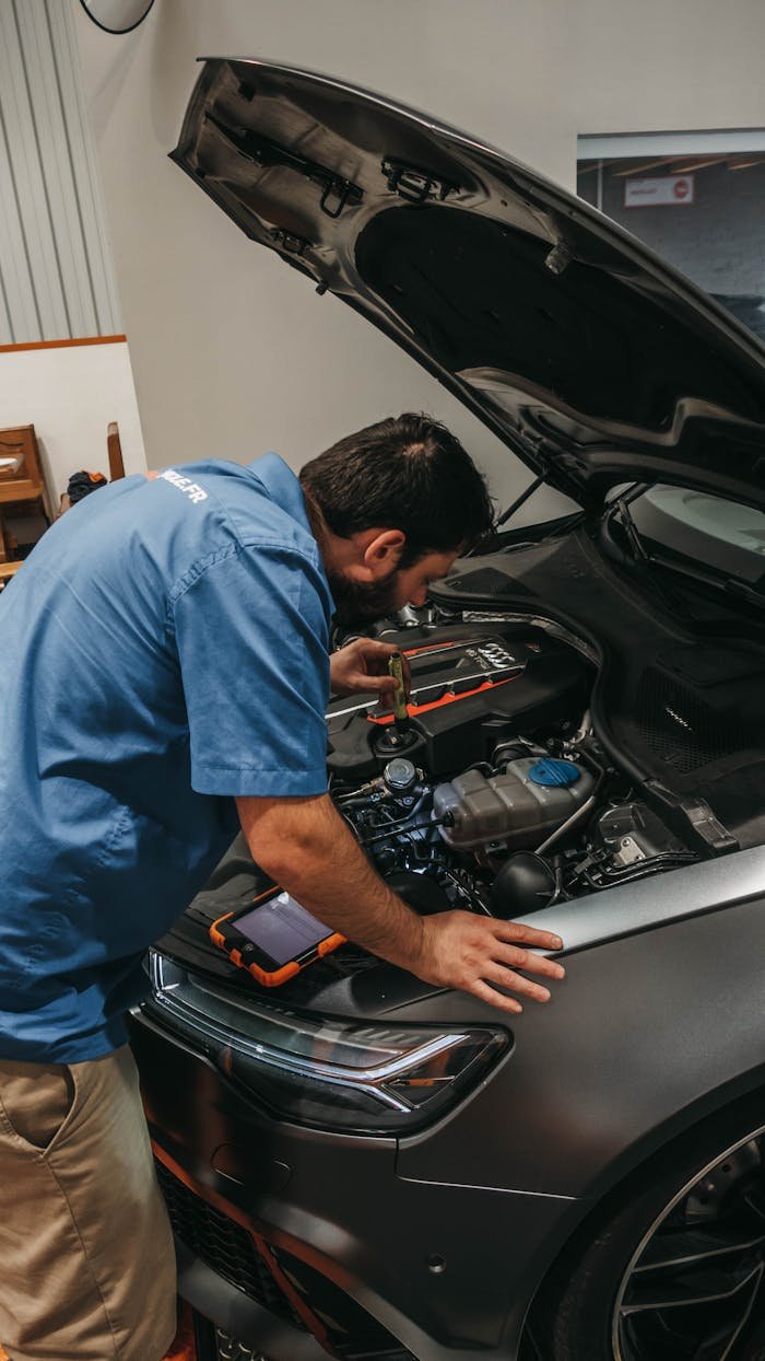 Mechanic in a workshop examining a car's engine under an open hood.